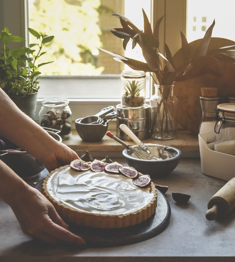 Woman hand holding homemade cheesecake with figs at kitchen background with window and natural light