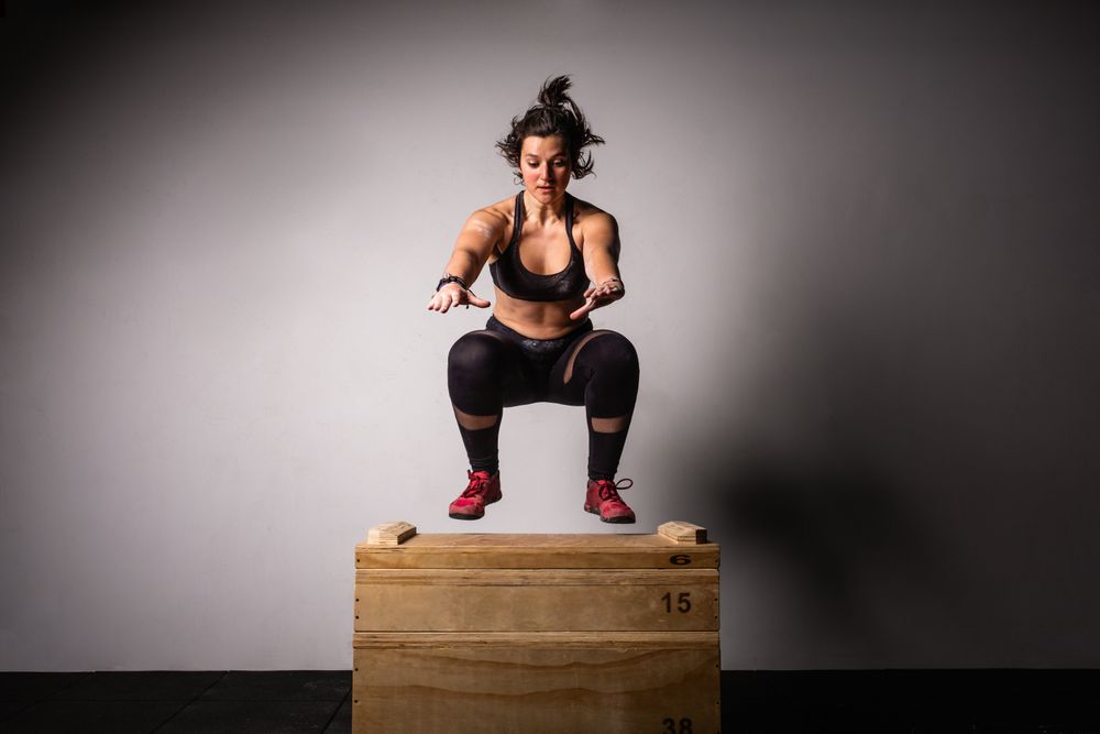 Woman jumping on wooden box in gym