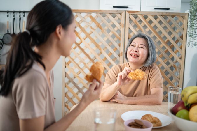 Mature mother and adult daughter enjoying croissants at home