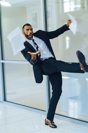 Untroubled businessman in suit and tie throwing papers in the air in office