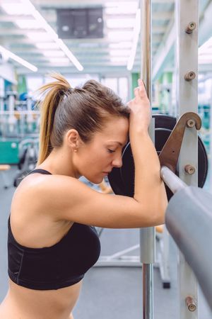 Fit brunette woman leaning on barbell in between lifting