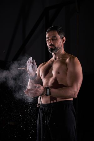 Muscular sportsman clapping hands with magnesium while preparing
