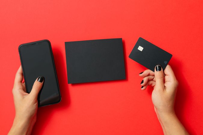 Female hands hold phone and card on red background, space for text