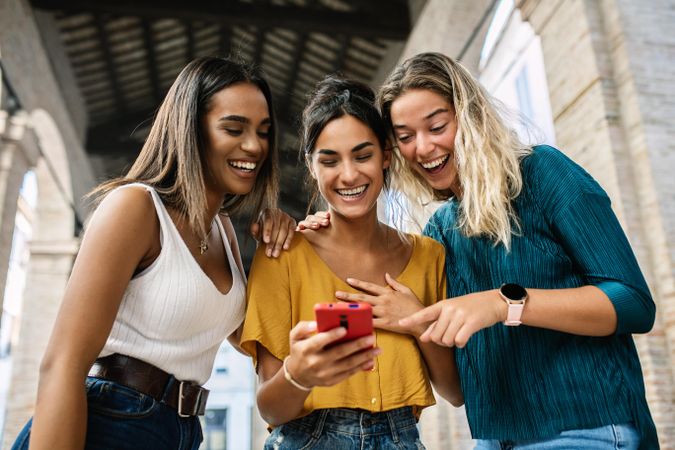 Laughing female friends gathered around a phone and laughing