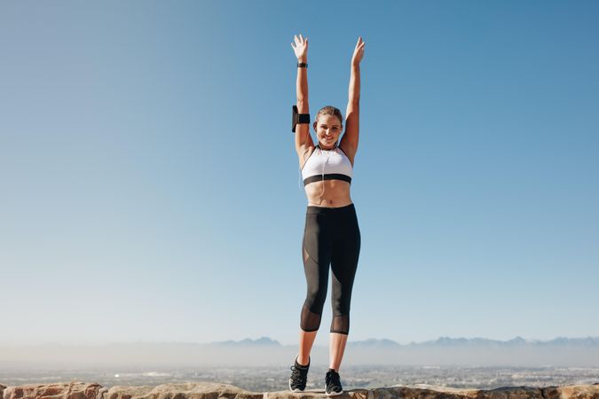 Accomplished runner raising arms as she reaches top of mountain