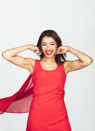 Portrait of a young fashion woman in red dress posing with her arms raised above her head