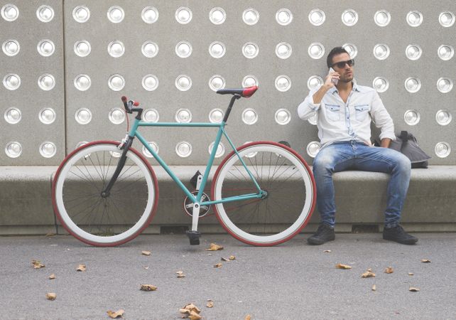Male speaking on phone while sitting with bike parked in front of patterned cement wall