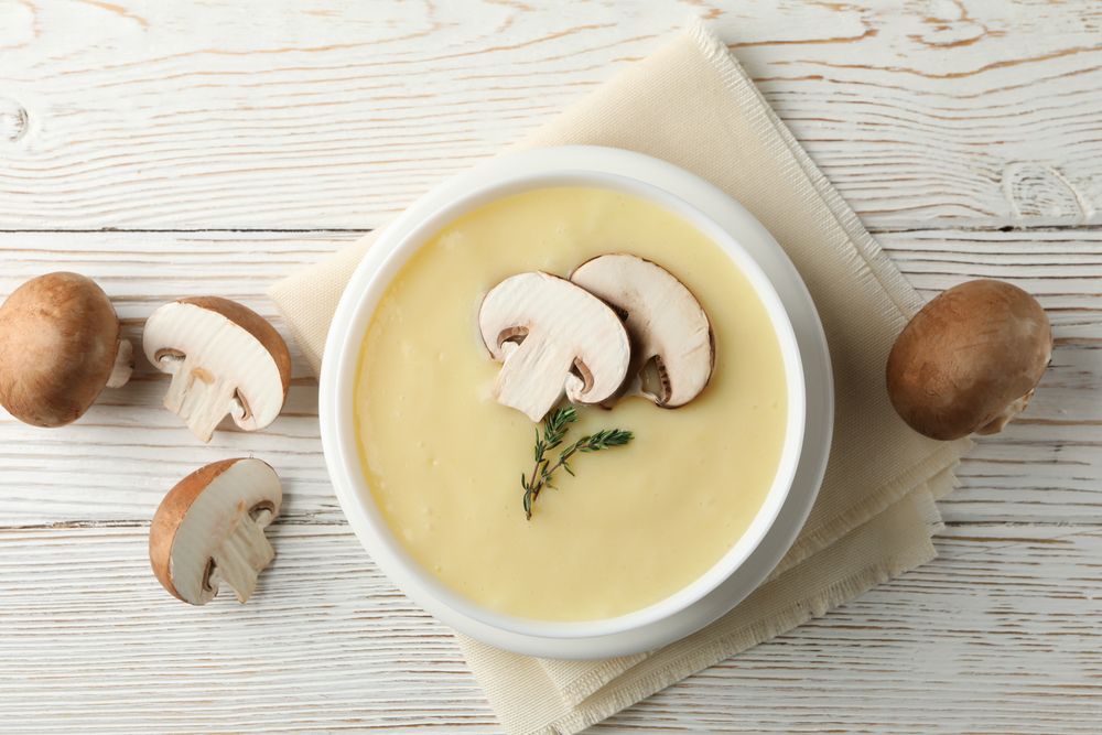 Looking down at bowl of creamy mushroom soup with herbs on napkin on wooden table