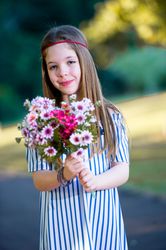 Smiling girl in blue striped dress holding a bouquet of flowers standing outdoor