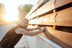 Mature man stretching on wooden wall in street