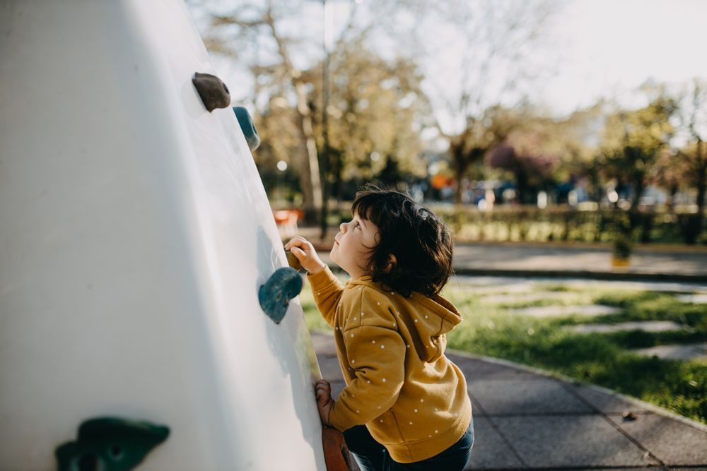 Young girl climbing small rock climbing wall in a park