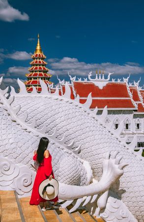 Woman wearing red dress standing beside light dragon statue at the exterior of Wat Huay Pla Kang temple in Thailand