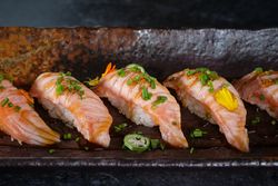 Appetizing nigiri sushi with salmon slices garnished with fresh herbs served on dark plate