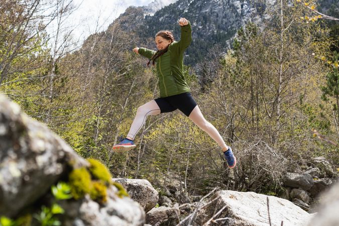 Carefree traveling woman jumping over river in mountains