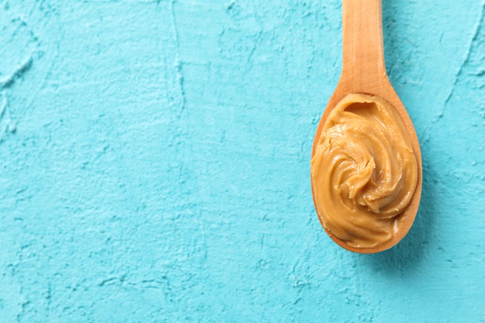 Spoon with peanut butter on color background, space for text and top view