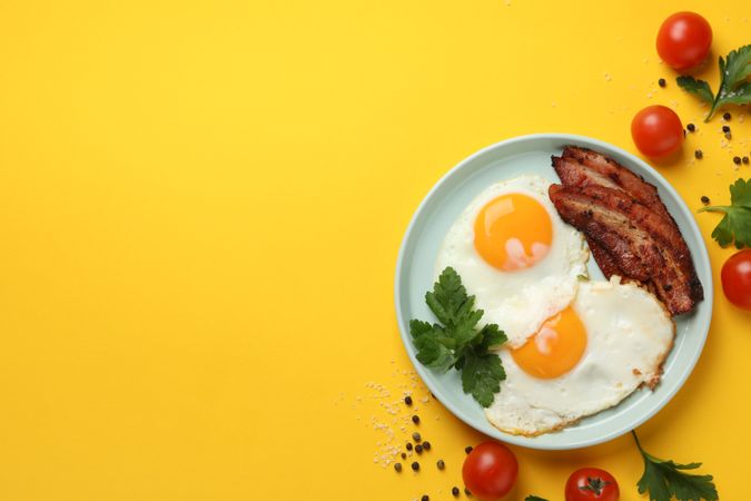 Looking down at plate of breakfast with eggs, sunny side up with bacon, copy space