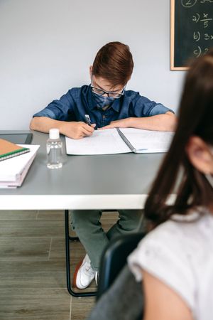 Boy with face mask writing at school