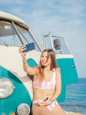 Woman taking selfie on smartphone at car on beach
