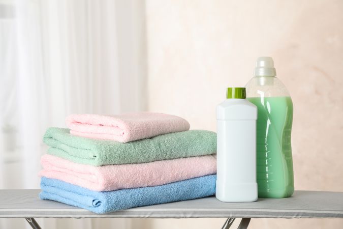 Stack of clean towels and laundry liquid on ironing board, copy space