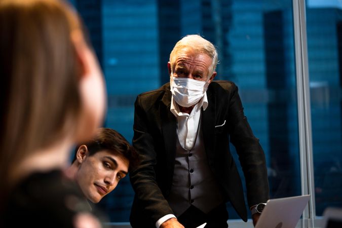 Mature man in protective mask discussing projects with employees