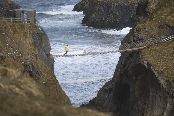 Tourist walking on rope bridge suspended between cliffs in Northern Ireland