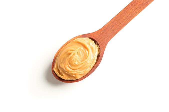 Creamy peanut butter in wooden spoon isolated on bright background, top view. A traditional product of American cuisine