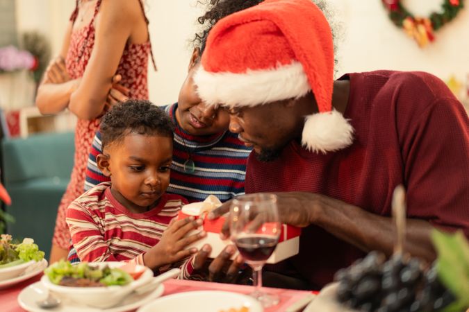 Black family is opening a Christmas gift together at the dinner table.
