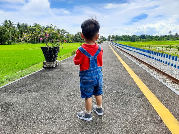 A toddler boy stands on the train station platform waiting for the arrival of a passenger train