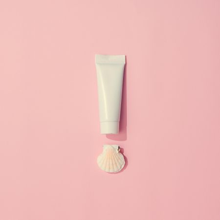 Sunscreen and shell on pastel pink background