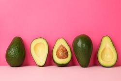 Ripe fresh avocado on pink background, space for text