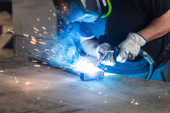 Welder in protective helmet welding metal detail in workshop