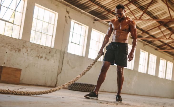Fitness man with battle rope in old warehouse