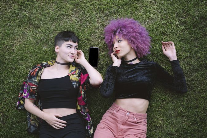 Women in colorful shirt and with pink hair lying on grass