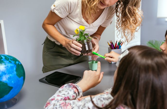 Female students pointing to a pansy roots holding by teacher hands in ecology classroom