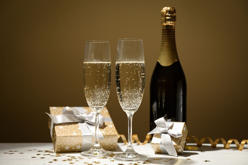 Gifts, champagne glasses and bottle on golden background, space for text