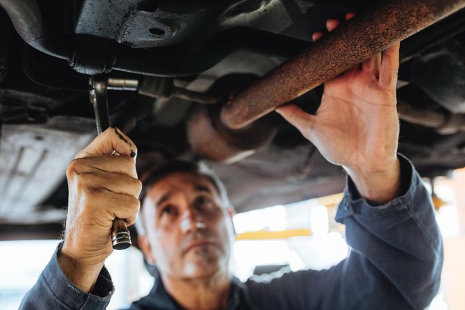 Car mechanic tightening exhaust system pipe under the car