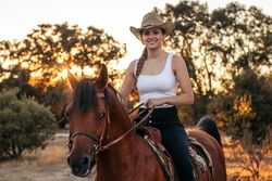 Young woman in hat riding a horse in the countryside at sunset