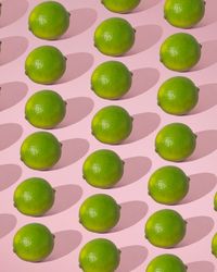 Rows of fresh limes on pink background with shadow
