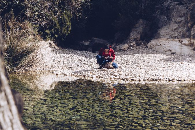 Positive woman resting on stone shore near river
