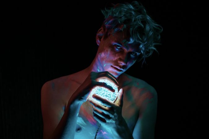 Topless young man carrying crystal ball lamp against dark background