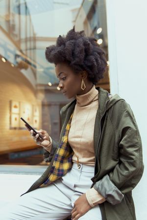 Young woman holding smartphone sitting beside window