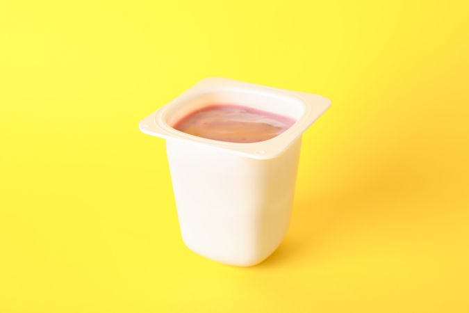 Plastic cup with yogurt on color background, space for text
