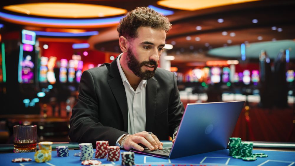 Portrait of a Young Man on Casino Floor, Using Laptop Computer to Play Online Casino Betting Jackpot Games.