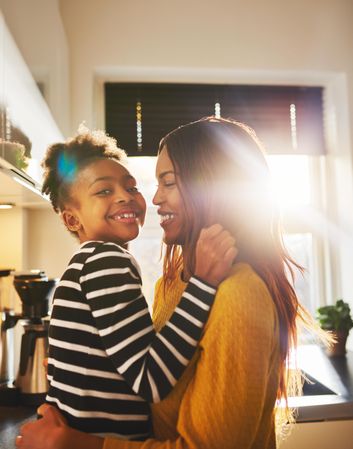 Mother holds daughter up in a sunny kitchen