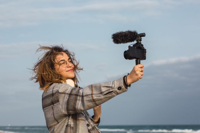 Young woman on seashore and shooting video on camera