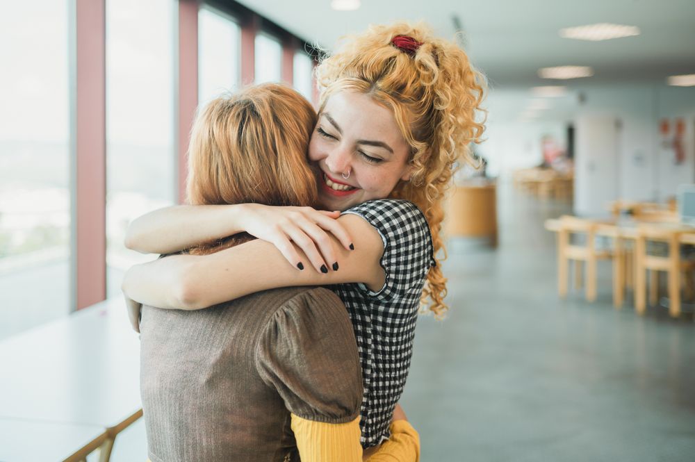 Happy teen students hugging in library