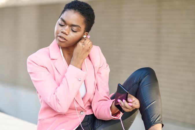 Female wearing suit with pink jacket putting in earbuds