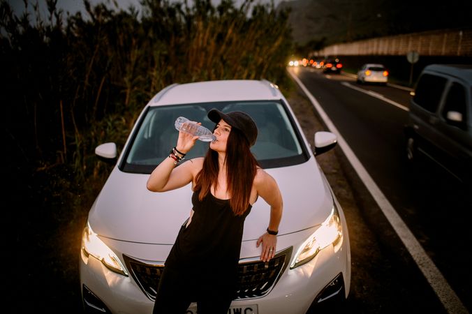Woman drinking water near car on road at night
