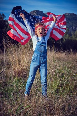 Smiling preteen boy in jeans overall standing in grassy meadow w