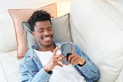 Cheerful Black man using smartphone on couch